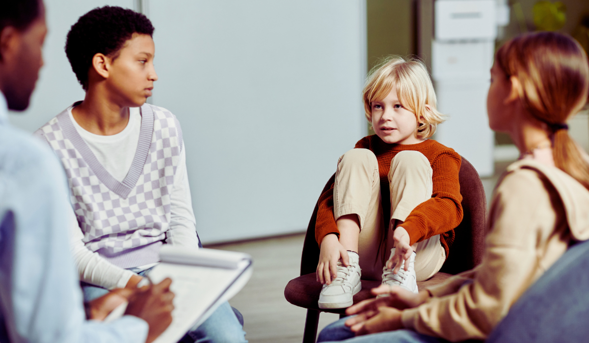 3 kids of varying ages sit in a therapy circle with a therapist.
