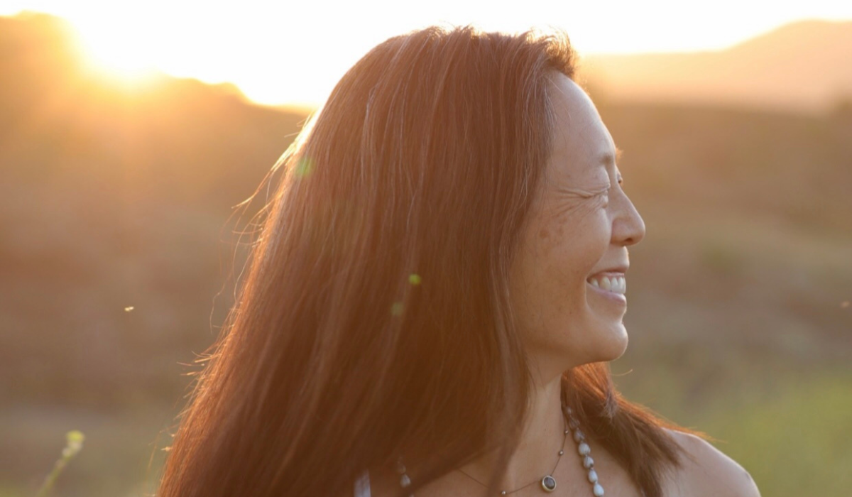 Wanda Wen with long, flowing hair stands in front of a bright sunset, with soft lighting creating a serene and dreamy atmosphere