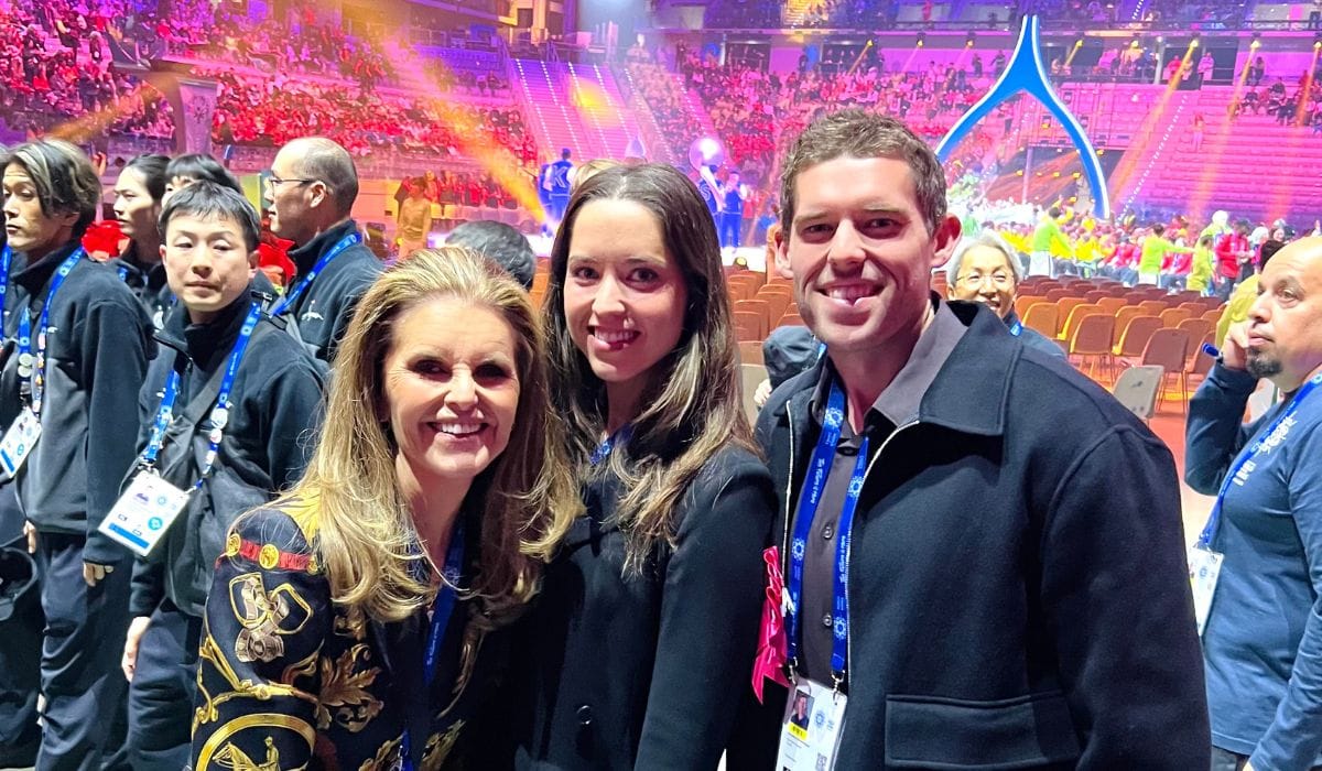 A group of event attendees poses for a photo in a brightly lit arena filled with cheering spectators in the background