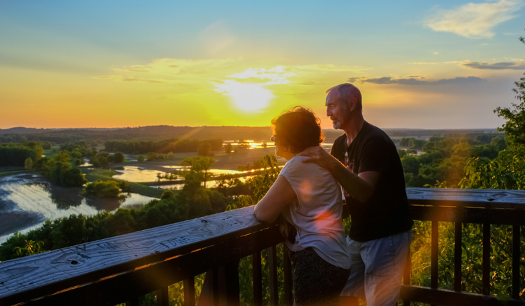 Man and woman on a wood deck overlooking a scenic view.